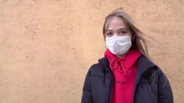 Kız, yüzünde koruyucu steril tıbbi maske takmış genç bir kadın dışarıdaki kameraya, sokak gösterisine, eldivenli ele bakıyor, dur işareti yok. Hava kirliliği, virüs, Çin salgını koronavirüs konsepti