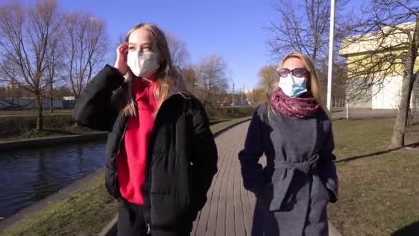 2人の親友の女の子が隔離と隔離の間に川の泉を散歩した 春には医療用マスクで公園を歩く Covidコロナウイルス感染からの保護の概念 — ストック動画