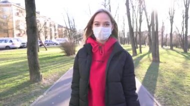 Yüz maskeli kız konuşmak için cep telefonunu kullanıyor. COVID Coronavirüs Salgını. Kadınlar güneşli bir günde parkta yürürken cep telefonu kullanırlar. 4K kirliliğinden ve virüsten korumak için maske