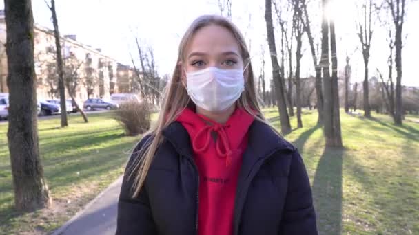 フェイスマスクの女の子は話すためにモバイルAを使用します Covidコロナウイルスパンデミックアウトブレイク 女は晴れた日に公園を散歩しながら携帯電話を使う ウイルスや汚染から守るマスク — ストック動画