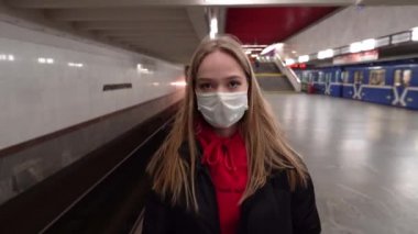 Tıbbi maske takmış genç bir sarışının portresi. Trafiğin en yoğun olduğu saatte metroda yürüyor. Hareket kısıtlaması. Olağanüstü hal. COVID-19 4K