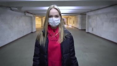 Koruyucu maskeli bir kız, halka açık bir yerde metro metrosunun altında insanların olmadığı bir yerden karşıya geçiyor. Halka açık yerlerde ve ulaşım şehrinde enfeksiyon. Sağlık karantinası ve güvenlik karantinası 4k