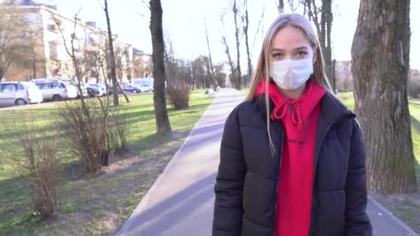 彼女の顔に保護滅菌医療用マスクの少女は 公園内の路上ショーヤシの屋外でカメラを見て 手袋をはめた手で 兆候を停止します 大気汚染 ウイルス 中国のパンデミックコロナウイルスの概念4K — ストック動画