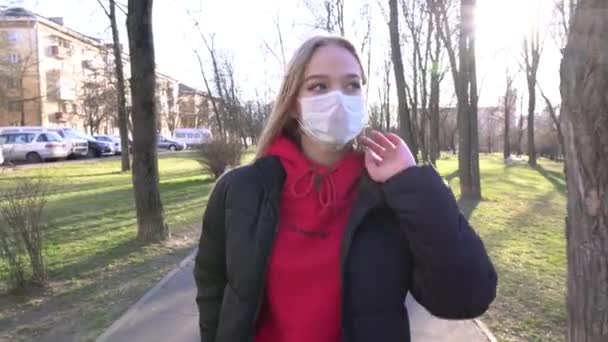 フェイスマスクの女の子は話すためにモバイルAを使用します Covidコロナウイルスパンデミックアウトブレイク 女は晴れた日に公園を散歩しながら携帯電話を使う ウイルスや汚染から守るマスク — ストック動画