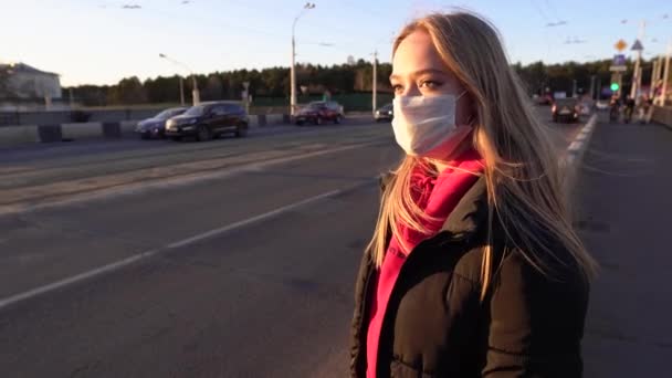 夕暮れ時に街中を通り過ぎる車の上に顔のマスクの美しい少女 パンデミック時に保護マスクを着用する意識的な市民 Covid 隔離4K — ストック動画