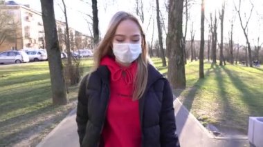 Yüz maskeli kız konuşmak için cep telefonunu kullanıyor. COVID Coronavirüs Salgını. Kadınlar güneşli bir günde parkta yürürken cep telefonu kullanırlar. 4K kirliliğinden ve virüsten korumak için maske