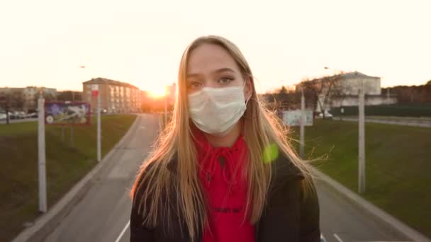 市内の医療用マスクの若い女性は 背景に鮮やかなコロナウイルスの保護パンデミック都市のスローモーション屋外に日没の太陽の下でマスクを着用 コロノウイルス検疫閉じるポートレート4K — ストック動画