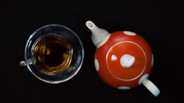 茶道一只雄性手在玻璃杯旁边用鲜花擦拭热玻璃杯红波尔卡圆点陶瓷茶壶中的碗。黑色背景，迎面而来的光4k — 图库视频影像