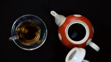 Çay seremonisi. Bir erkek el, cam bir kase için cam kasenin yanındaki sıcak kırmızı, beyaz seramik çaydanlığın seramik kapağını kapatır. Siyah arkaplan, gelen ışık 4k