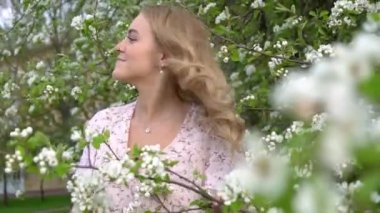 Güzel Sakura bahçesinde uzun sarı saçlı çekici bir kadın. Çiçek açan ağaçlarda mutlu güzel bir kız. Güzel sarışın kız çiçek açan ağaç dallarında beyaz çiçeklerle poz veriyor.