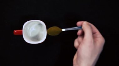 Bir kaşık dolusu kahve. Kahve tozu kaşıktan yavaş çekimde düşüyor. Siyah arka planda kırmızı bir fincanda metal bir kaşığa kahve dök.