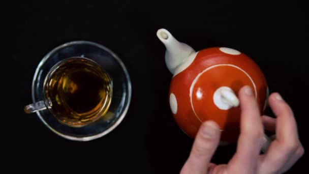 Çay seremonisi. Bir erkek el, cam bir kase için cam bir kasenin yanındaki sıcak kırmızı seramik çaydanlığın seramik kapağını açar ve kapatır. Siyah arkaplan, gelen ışık 4k — Stok video