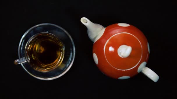 Çay seremonisi. Bir erkek el, cam bir kase için cam kasenin yanındaki sıcak kırmızı, beyaz seramik çaydanlığın seramik kapağını açar. Siyah arkaplan, gelen ışık 4k — Stok video