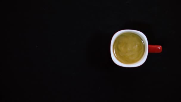Bovenaanzicht van roeren koffie met lepel. Melk en koffie. Een cappuccino. Geweldige macro shot van het gieten van verse melk in een glazen mok met koffie of thee erin. zwarte achtergrond 4k — Stockvideo
