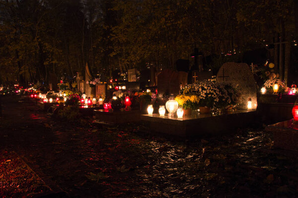 Flaming candles on the graves in cemetery during All saints day at night.