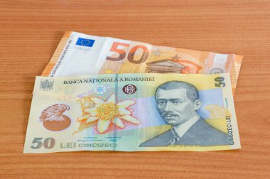 Tahta masanın üzerinde 50 Euro banknot (EUR) ve 50 Romanya lei banknotu (RON).