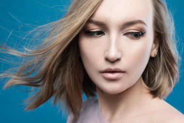 Temiz ciltli güzel bir genç kadın. Doğal çıplak makyajlı ve yüzüne dokunan güzellik modeli portresi. Spa, cilt bakımı ve sağlık. Kapat, mavi arkaplan, kopyala alanı.