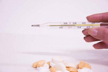 Kızın elini yüksek vücut sıcaklığı gösterir bir termometre tutar. Çok renkli hapları antibiyotik ön planda. Mevsimlik hastalık, zayıf bağışıklık. Beyaz arka plan.