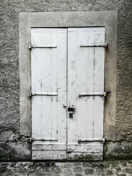 Vintage painted white wood double door with stucco frame, strap hinges, and padlock with a rustic and worn look and cobblestone road in foreground