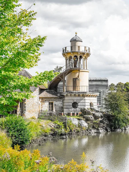 Wunderschöner Leuchtturm mit Wrap-around-Treppe und Aussichtsplattformen mit Blick auf einen Teich in Versailles Frankreich mit weißen flauschigen Wolken am Himmel über. — Stockfoto