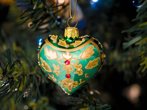 一个绿色和黄色的手绘玻璃饰品的照片 在一个美丽的节日背景下 晚上在一棵人工点燃的圣诞树上挂着一只听到的图片 — 图库照片