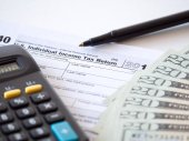 Close-up fotografii kopie individuální daňové přiznání s černými Kalkulačka a 20 dolarové bankovky pročesávat zástupce Spojených států federální daňové škrty a úspory v tomto roce.