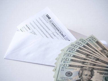 Fotoğraf 20 dolar faturaları yığını ve vergi indirimi tasarruf temsil eden bir posta zarf ile hazine bireysel gelir vergisi beyannamesi formunun 1040 federal bölümünün kapatın.