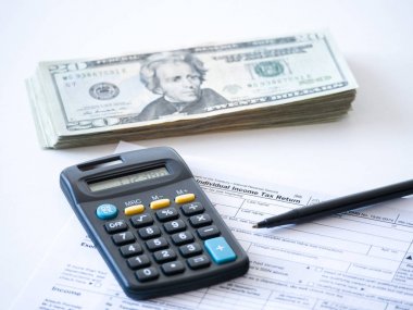 Close-up photograph of a hard copy of an individual income tax return with black calculator and 20 dollar bills piled up representative of United States federal tax cuts and savings this year. clipart