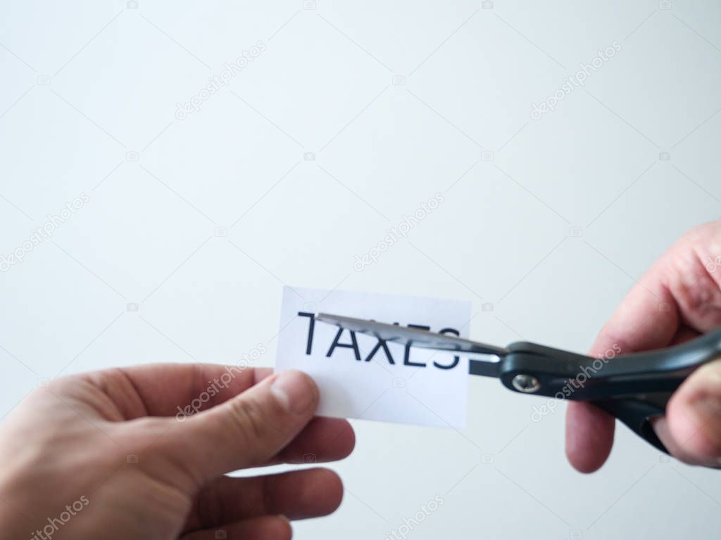 Closeup photograph of man holding black handle scissors and cutting a paper with the word taxes on it representative of federal and state tax cut reform saving people money with new deduction policy.
