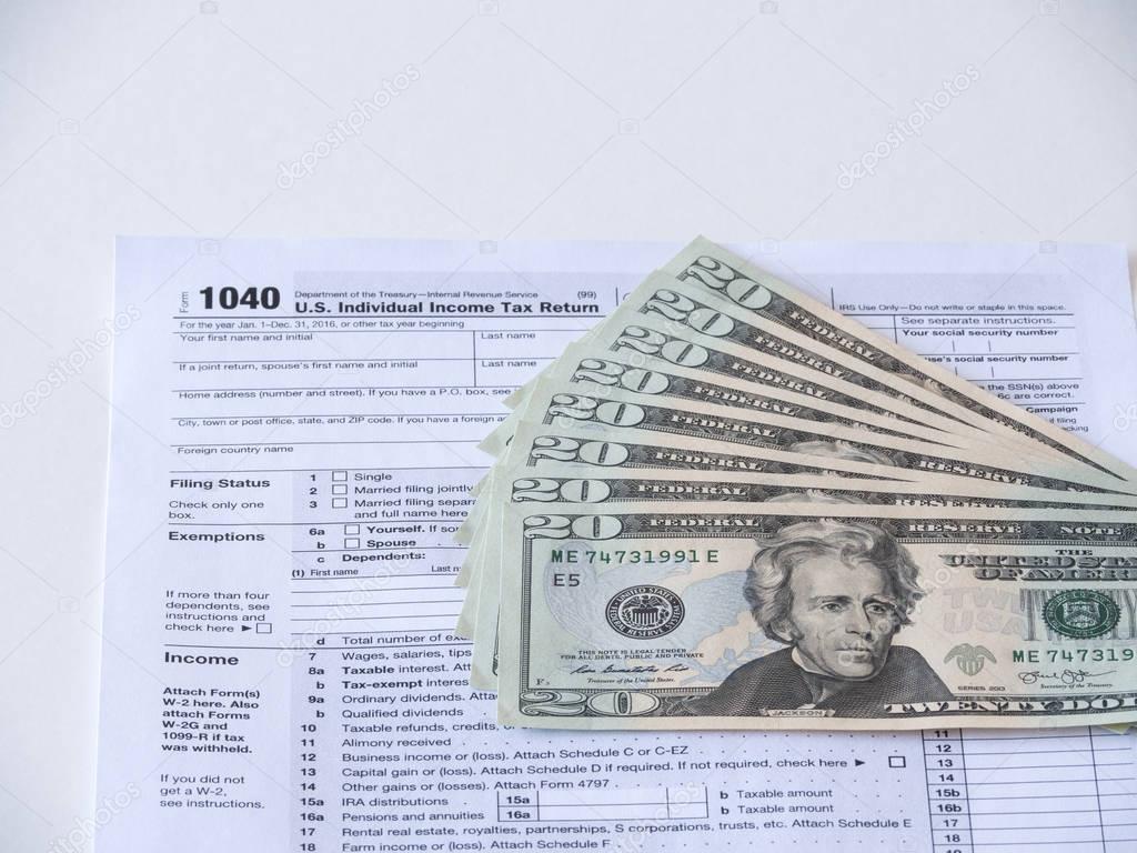 Close up photograph of 1040 individual earnings federal government department of treasury tax return with twenty dollar bills fanned out on top representative of tax deduction savings or fees.