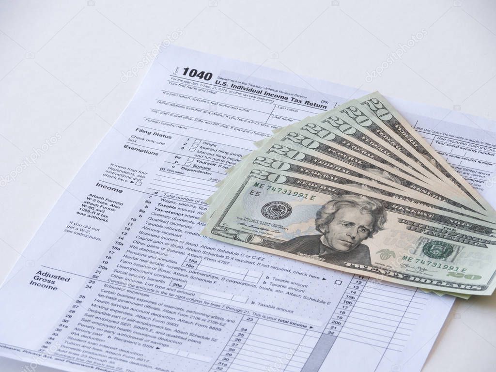 Close up photograph of 1040 individual earnings federal government department of treasury tax return with twenty dollar bills fanned out on top representative of tax deduction savings or fees.