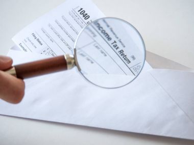 1040 federal hükümet bireysel gelir vergi iade formunun yakın plan fotoğrafı beyaz bir zarfın içinde, metni büyütmek için elinde büyüteç tutan bir adam var..