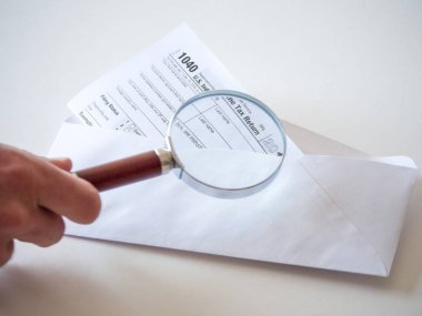 1040 federal hükümet bireysel gelir vergi iade formunun yakın plan fotoğrafı beyaz bir zarfın içinde, metni büyütmek için elinde büyüteç tutan bir adam var..