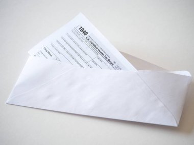 Üst vergi sezonu için zamanında posta hazırlanılıyor beyaz bir arka plan üzerinde çıkıntılı 1040 federal bireysel gelir vergisi beyannamesi formu basılı bir kopyasını ile açık zarf closeup görmek.