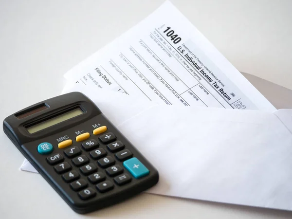Closeup image of a stuffed envelope with the federal 1040 individual income tax return with black calculator isolated on a  white background for tax season background or wallpaper.
