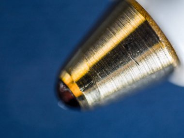 Tükenmez kalemle işlenmiş altın metal uç ve mürekkep dolu top ucu mavi bir arka plan üzerinde bir aşırı closeup makro ayrıntı mikroskobik görüntü.