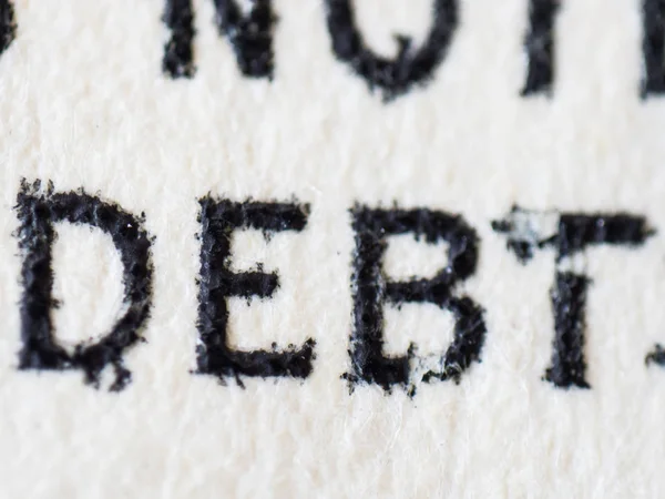 An extreme colored closeup macro detail microscopic image of printed currency showing printed text with the word debt in capital letters.