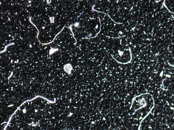 An extreme closeup macro detail microscopic image of dust molecules, particles, strings and strands on a black textured background.