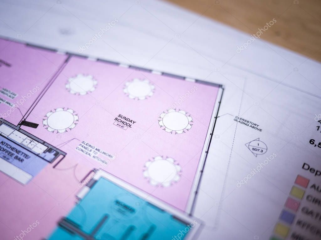 Photograph of generic colored architectural floor plan drawing printed on white paper set on top of a wood desk in a architect studio.