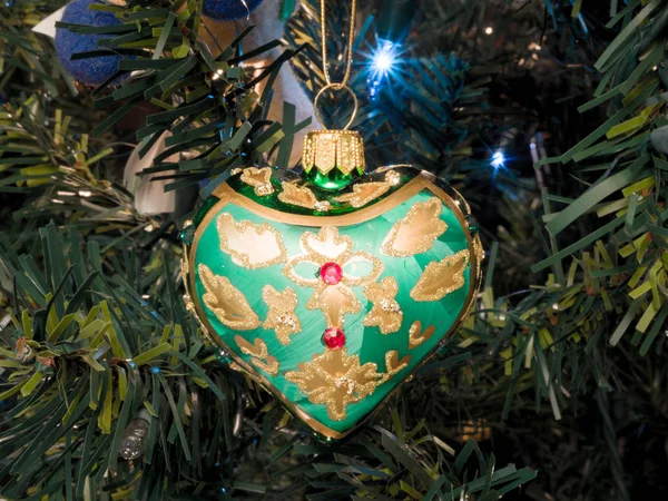 一个绿色和黄色的手绘玻璃饰品的照片 在一个美丽的节日背景下 晚上在一棵人工点燃的圣诞树上挂着一只听到的图片 — 图库照片