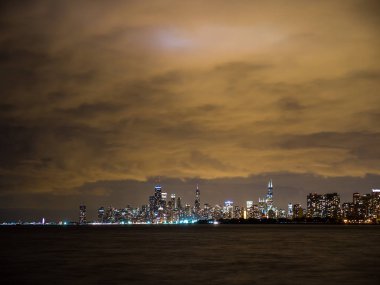 Sadece güneş battıktan sonra uzun pozlama fotoğraf ön plan ve yukarıda bulutlu gökyüzü Michigan Gölü ile Chicago şehir manzarası binalarda renkli ışıkların güzel gece zaman.
