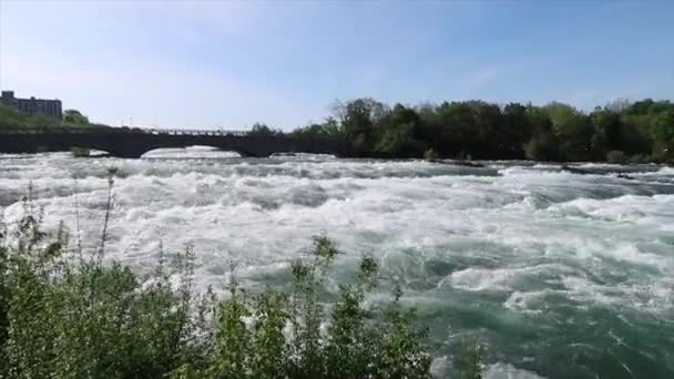 Posouvání zobrazení tekoucí vodě peřeje na řece Niagara před American Falls vodopád s Green Island a Goat Island v pozadí počínaje Goat Island bridge do Kanady za PDA. — Stock video