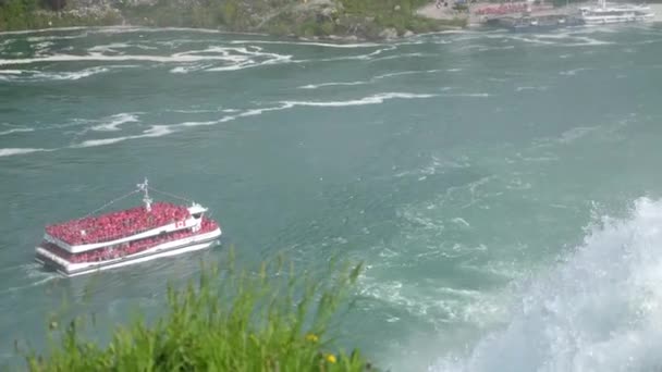 Niagara, NY - May 28th 2017: The Hornblower tour boat from the Canadian side retreat down stream on the Niagara river with the American Falls waterfall gushing over the cliff above . — стоковое видео