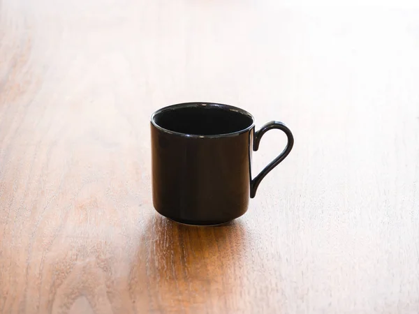 Close up background photograph of a single empty black porcelain or ceramic tea or coffee cup or mug isolated on a dark wood grain table and half heart shaped curved handles.