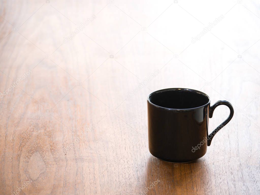 Close up background photograph of a single empty black porcelain or ceramic tea or coffee cup or mug isolated on a dark wood grain table and half heart shaped curved handles.