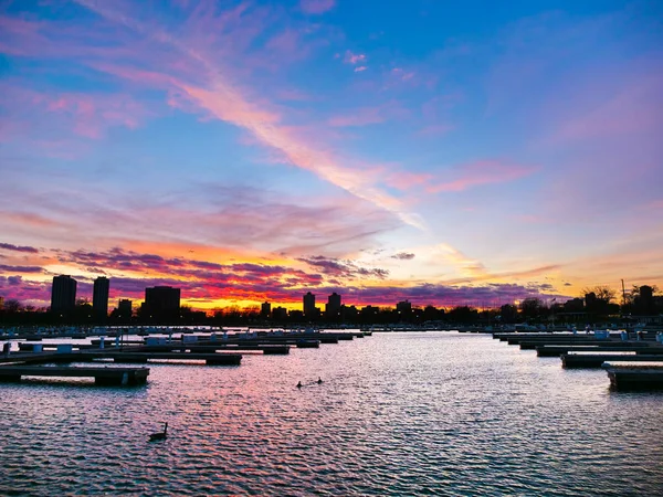 A breathtaking and vivid colorful landscape sunset photograph with beautiful pink, blue, yellow and orange colors over Montrose Harbor in Chicago with building silhouettes at the horizon.