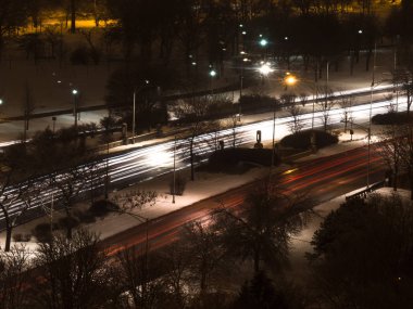 Long exposure photograph of car headlight and tail light streaks or trails on Lake Shore Drive in Chicago over foster beach underpass with speed limit sign and bare trees in snow covered ground. clipart