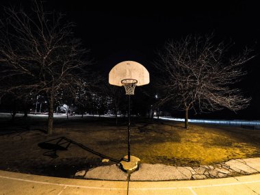 Gece fotoğrafı var, açık basketbol sahası ve Basketbol basketbol beyaz Potaların turuncu jantlar ve Chicago şehir sokak ışık yakın ile yaktı ağları ile yıpranmış.