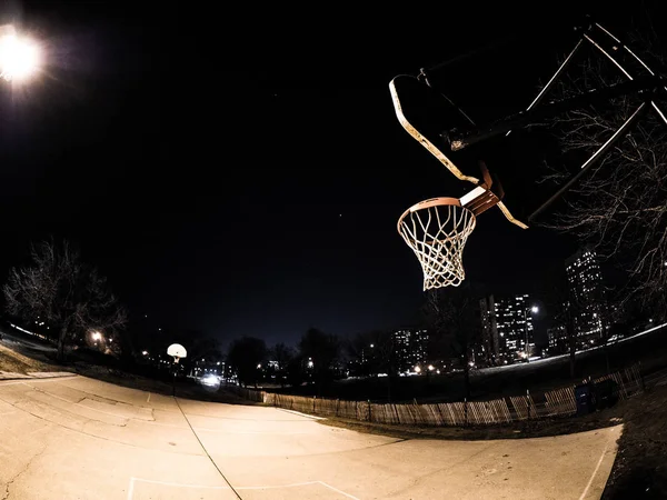 一张室外风化的篮球场和篮球篮的夜晚照片 白色的篮板橙色轮辋和网在芝加哥城附近的路灯照亮 — 图库照片