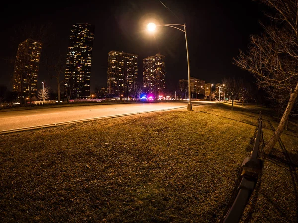 Beautiful long exposure night photograph of high rise residential condo buildings with grass in foreground and lights from nearby cops, firetrucks and ambulance on lake shore drive in Chicago.